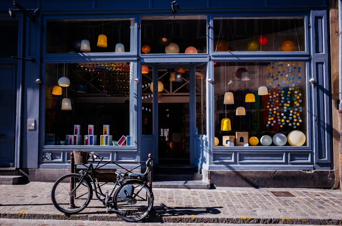 Fachada de uma loja de bairro com vitrine iluminada e bicicleta encostada na calçada.